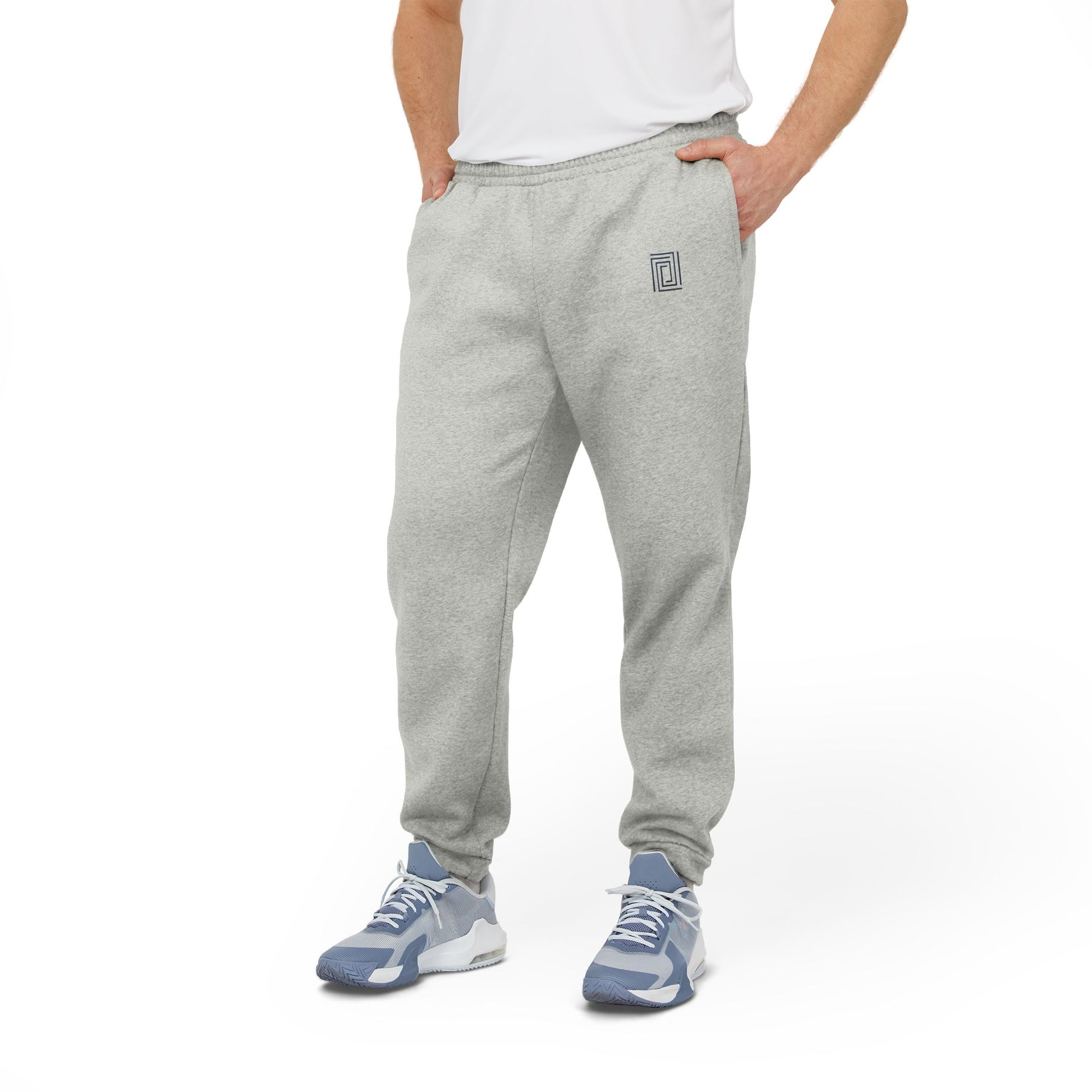 Model in gray Adidas fleece joggers, wearing a white t-shirt and stylish sneakers, standing confidently with hands in pockets.