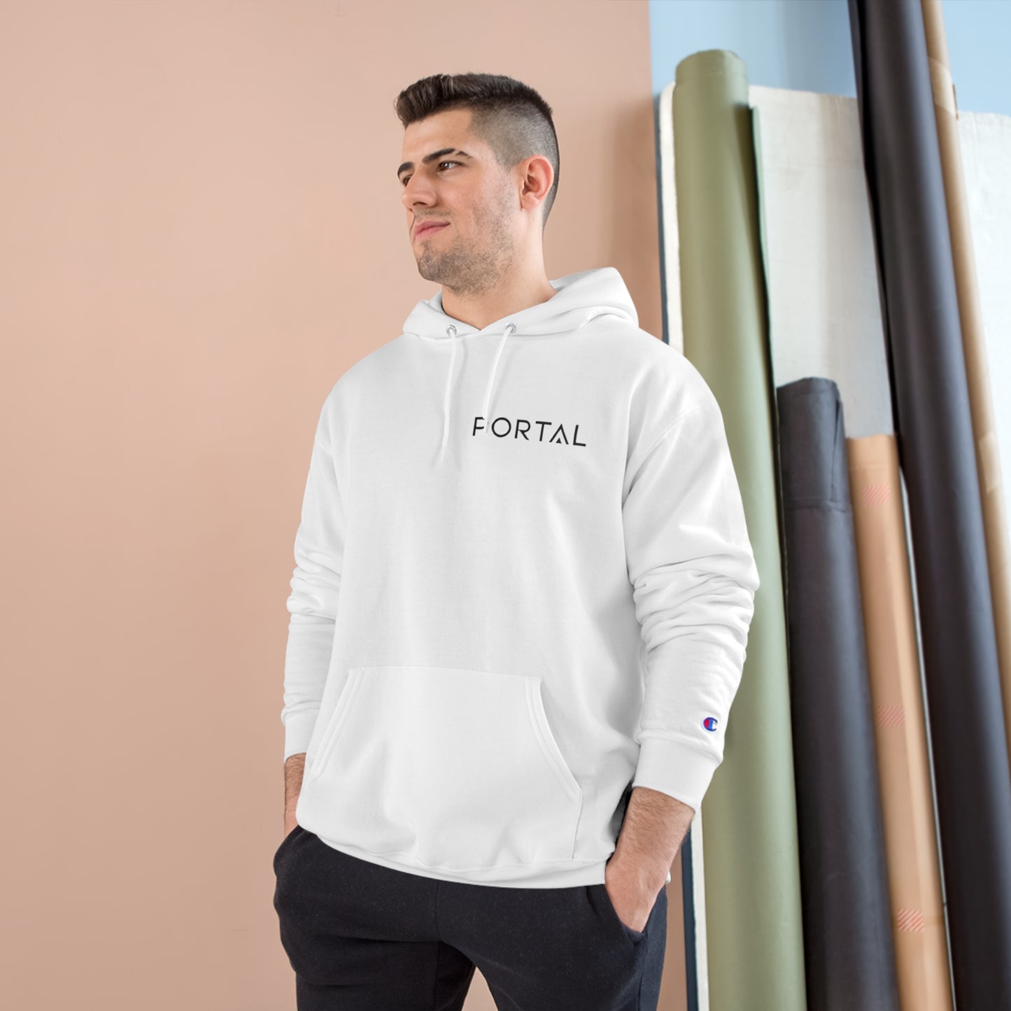 A man wearing the white Champion S700 Eco Hoodie with 'PORTAL' on the front, standing casually against a colorful backdrop.